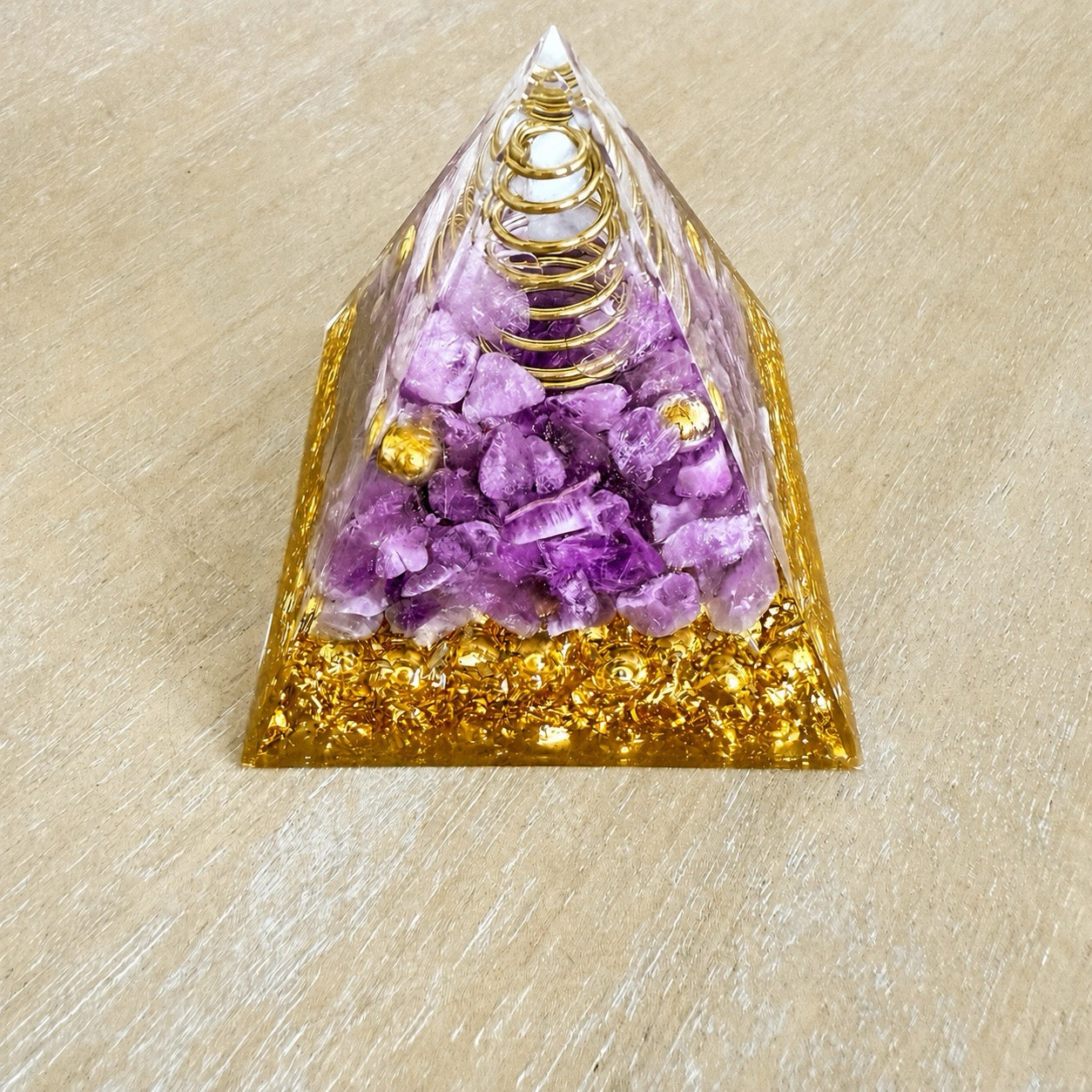 Gros plan pyramide orgonite améthyste avec bobine de fil doré, éclats de cristaux violets et base en résine dorée