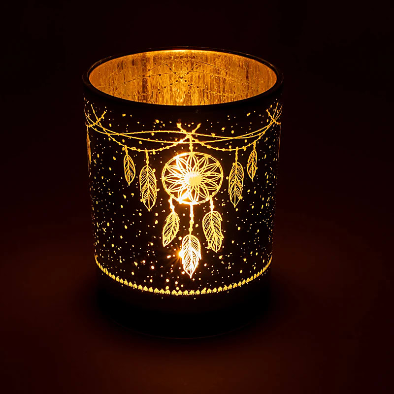 Photophore attrape-rêves illuminé par une bougie chauffe-plat, laissant apparaître le motif doré en transparence dans l'obscurité