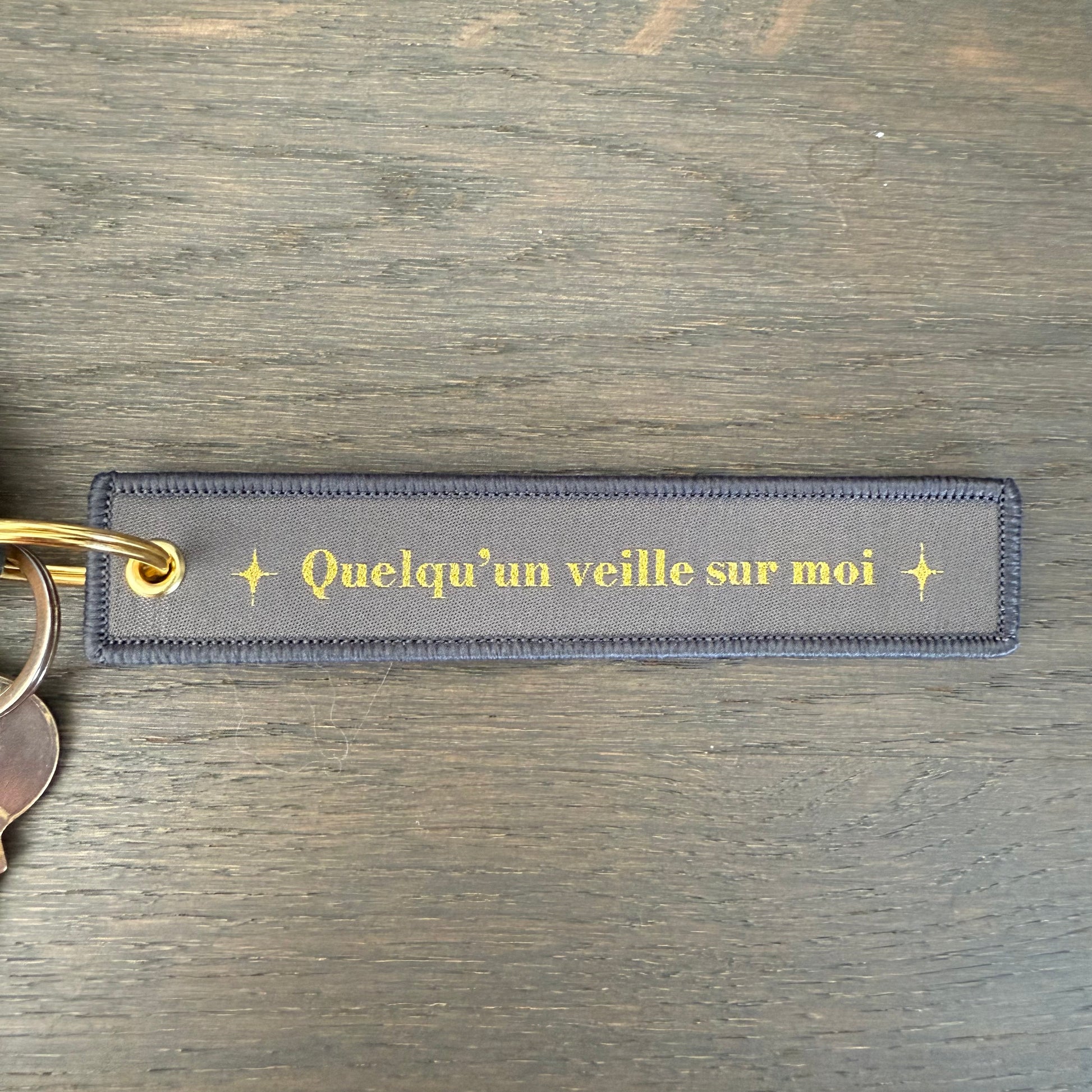 Porte clé en tissu gris avec message quelqu'un veille sur moi dorén mousqueton doré