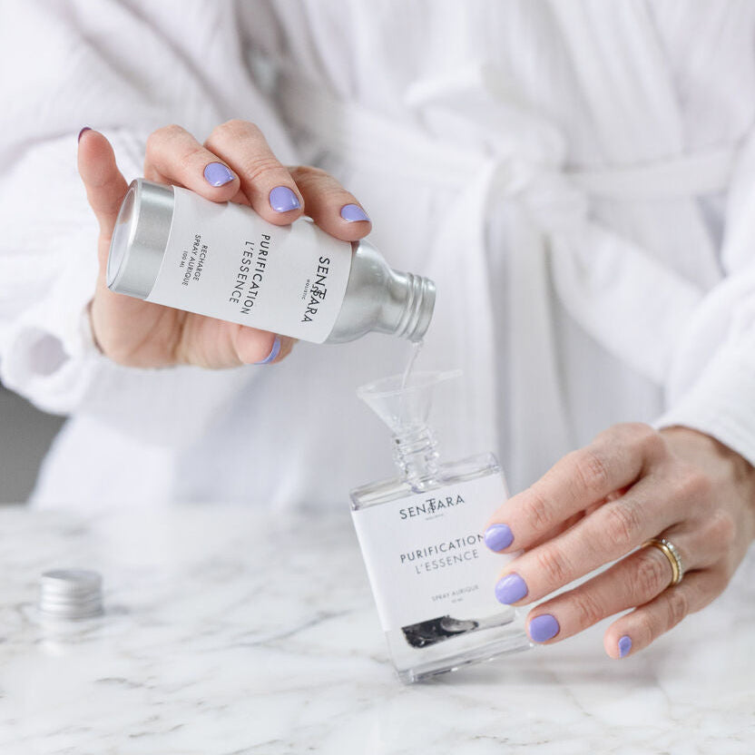 Mains de femmes versant la recharge de l'essence purification spray aurique Sentara Holistic dans la bouteille en verre d'origine, à l'aide d'un petit entonnoir