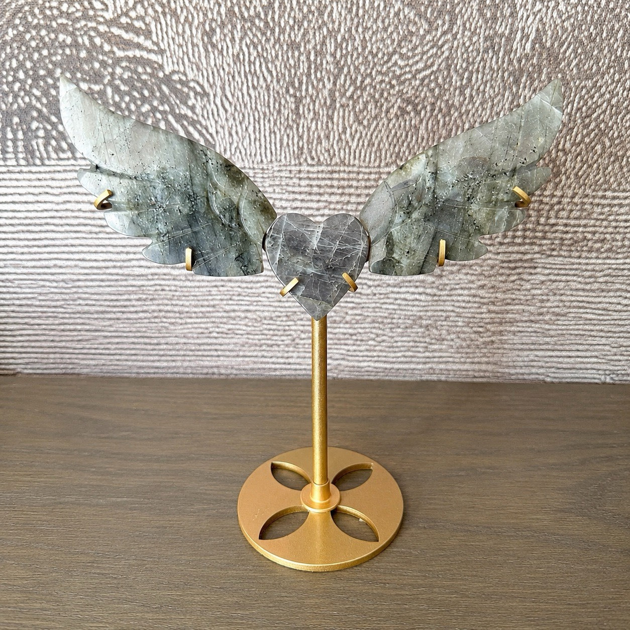 Sculpture en Labradorite grise véinée, cœur et ailes d'ange sur socle doré, vue de face, fond toile grise et étagère bois