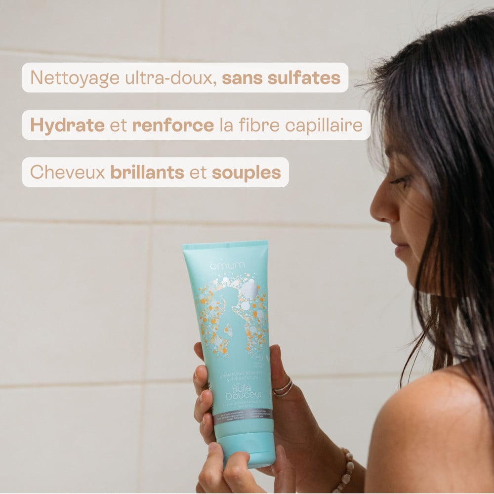 Visuel d'une femme dans sa salle de bain tenant le shampoing Ma bulle douceur d'Omum, inscriptions des bienfaits 