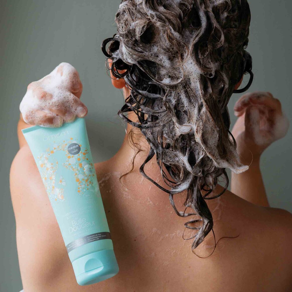 Femme de dos se lavant les cheveux avec le shampoing Ma bulle douceur d'Omum, mousse onctueuse