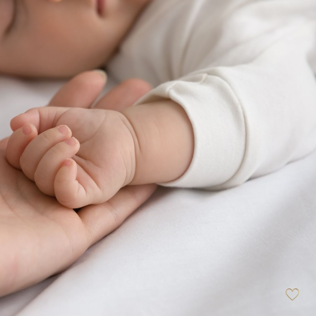 Bébé dormant sur le dos avec sa main droite posée dans une main de femme