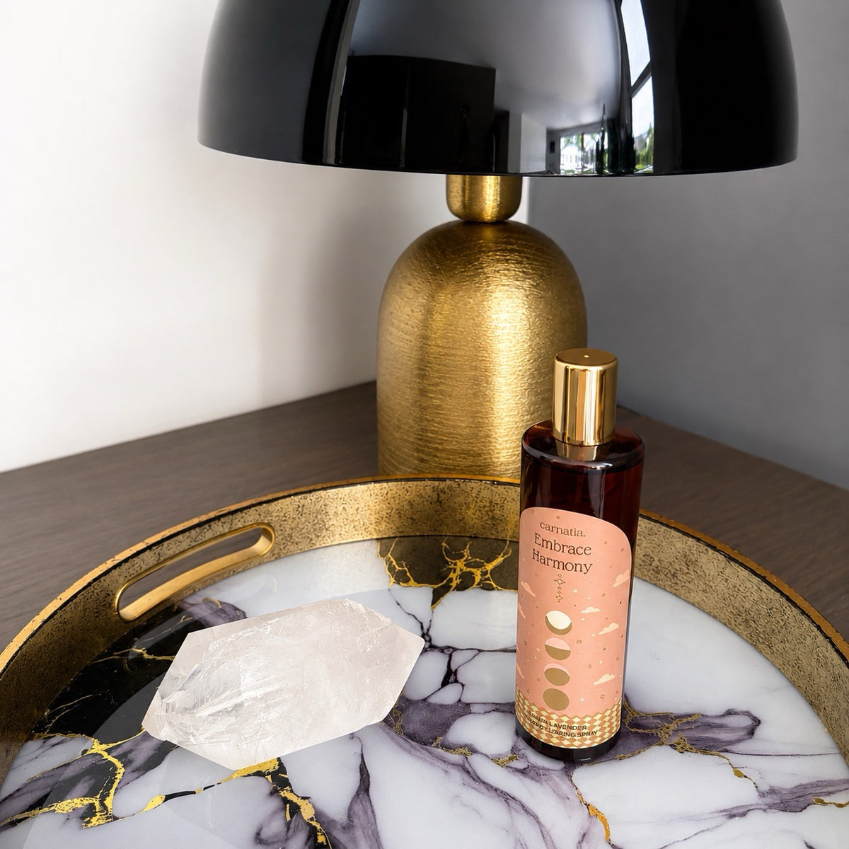Spray d'ambiance Embrace Harmony Lavande Lunaire Carnatia , flacon verre ambré et doré posé sur plateau marbré avec cristal de quartz, lampe dorée en arrière-plan
