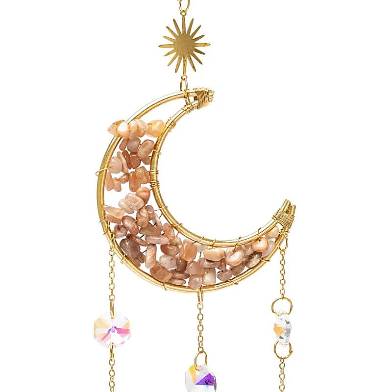 Focus sur un attrape-soleil doré en forme de croissant de lune, garni d'éclats de pierre de lune rose, avec trois chaînes pendantes ornées de soleils dorés et de pendentifs en cristal de roche facetté