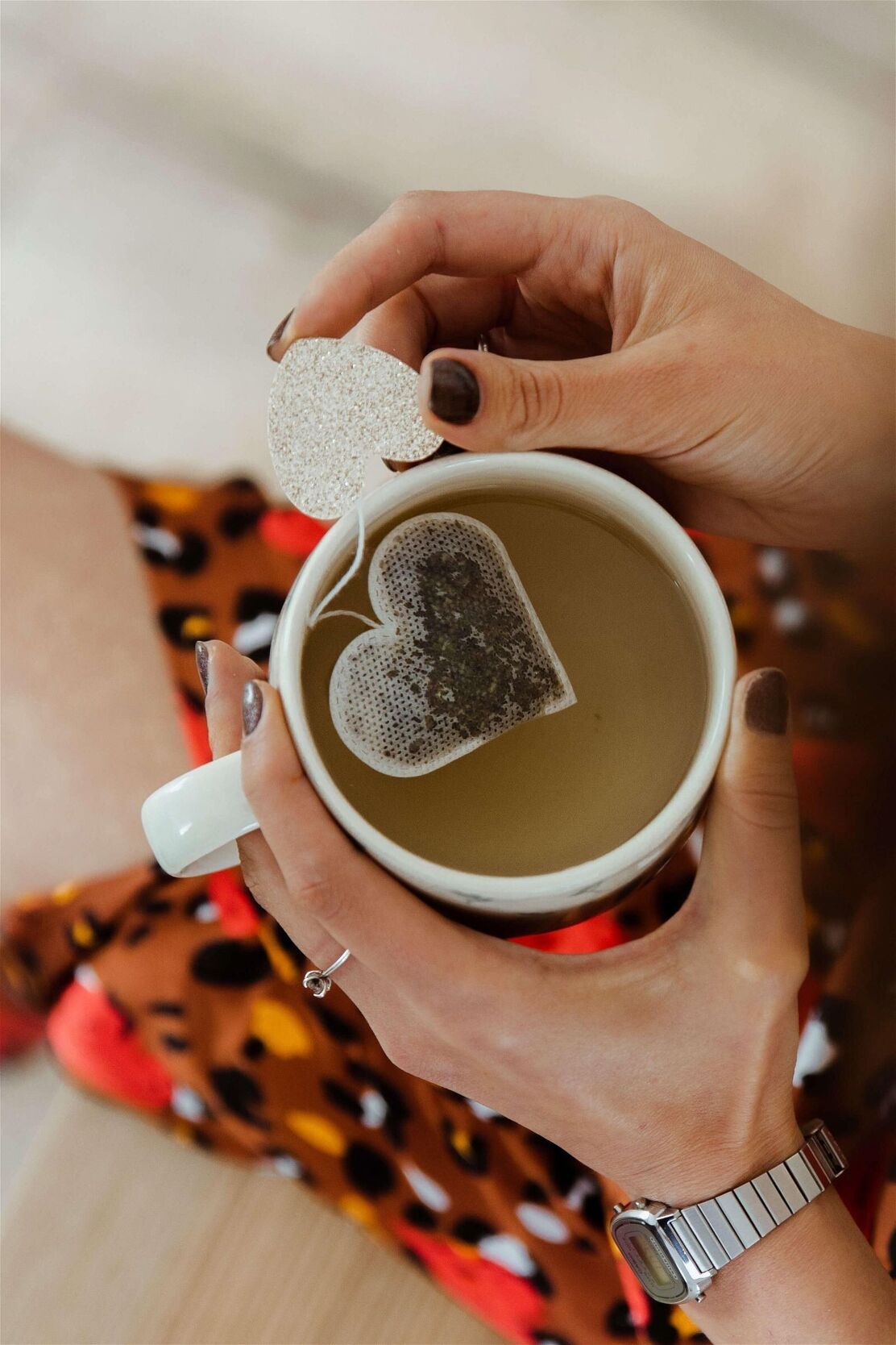 Mains de femme tenant une tasse de thé avec un sachet en forme de coeur relié par un fil en coton à une étique coeur pailletée