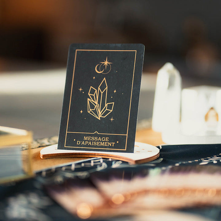 Carte oracle avec message d'apaisement, posée sur un socle en bois en forme de lune, cristal de roche en pointe dans le fond